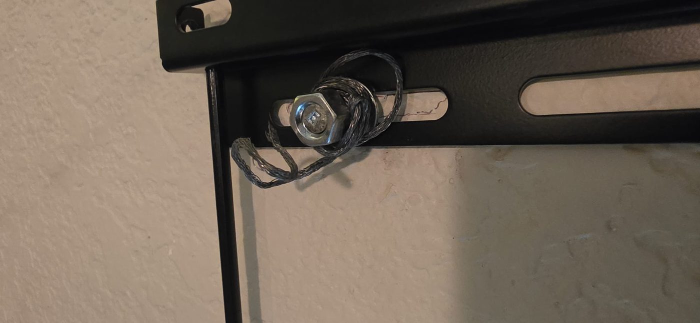 The bolt holding a television to the wall, with a piece of braided wire wrapped around it in place of a washer