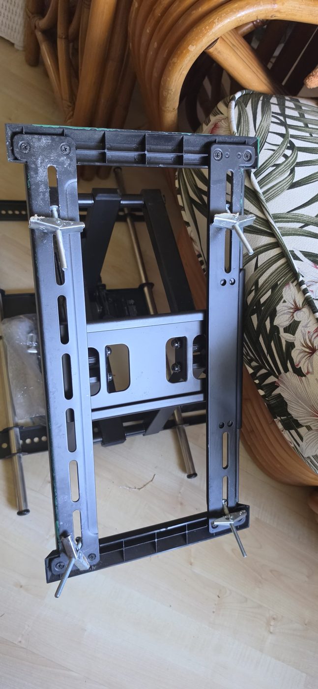 An articulating TV mount taken off the wall with its butterfly anchors still threaded through the bracket